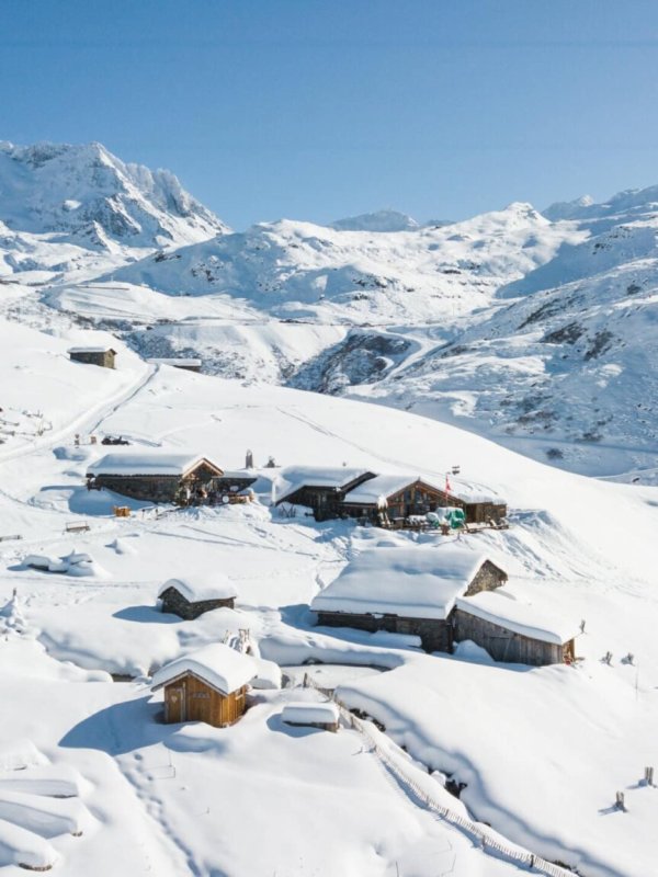 Chalets de Chez Pépé Nicolas sous la neige, avec le jardin en rosace au premier plan et les sommets enneigés sous un ciel bleu.