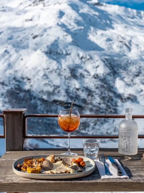 Assiette et cocktail sur la terrasse de Chez Pépé Nicolas, face aux montagnes enneigées de la vallée des Belleville.
